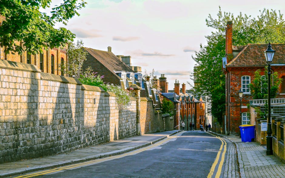 A narrow alleyway between two brick buildings, with a slightly wet pavement marked by double yellow lines on each side. At the far end of the alley, a small wooden staircase leads up to a doorway on t